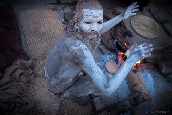 Naga sadhu warming himself next to a fire.