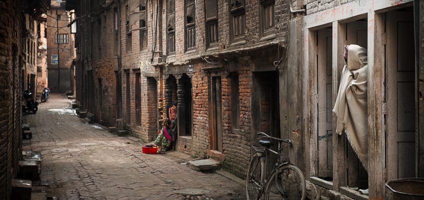 A small alley with a man, a woman and a bicycle on a brick-lined road.