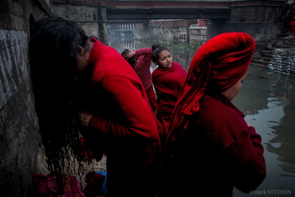 Hindu pilgrims wearing red robes and drying themselves after a holy bath.